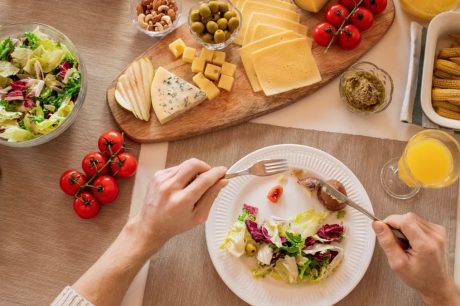 Overhead view of a cheese platter with fresh salad and juice, perfect for a gourmet lunch setting.